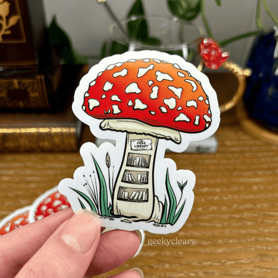 Fantasy sticker of a tiny, free library inside of a mushroom for readers held above a wooden desk with books and a potted plant in the background.