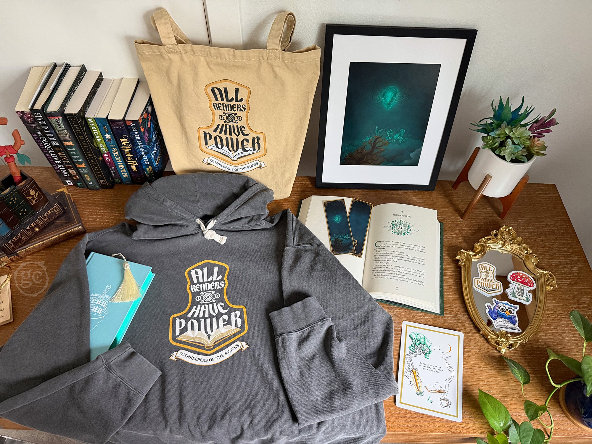 Gray hoodie with 'All Readers Have Power' design on a wooden surface with books and decor.