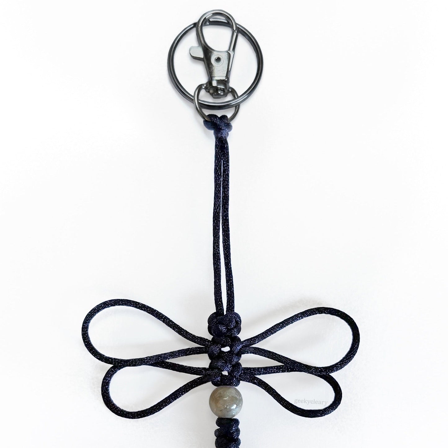 Close up of Nightwing Dragonfly Specimen keychain made of black silk cord, a real agate bead, and silver-toned hardware.