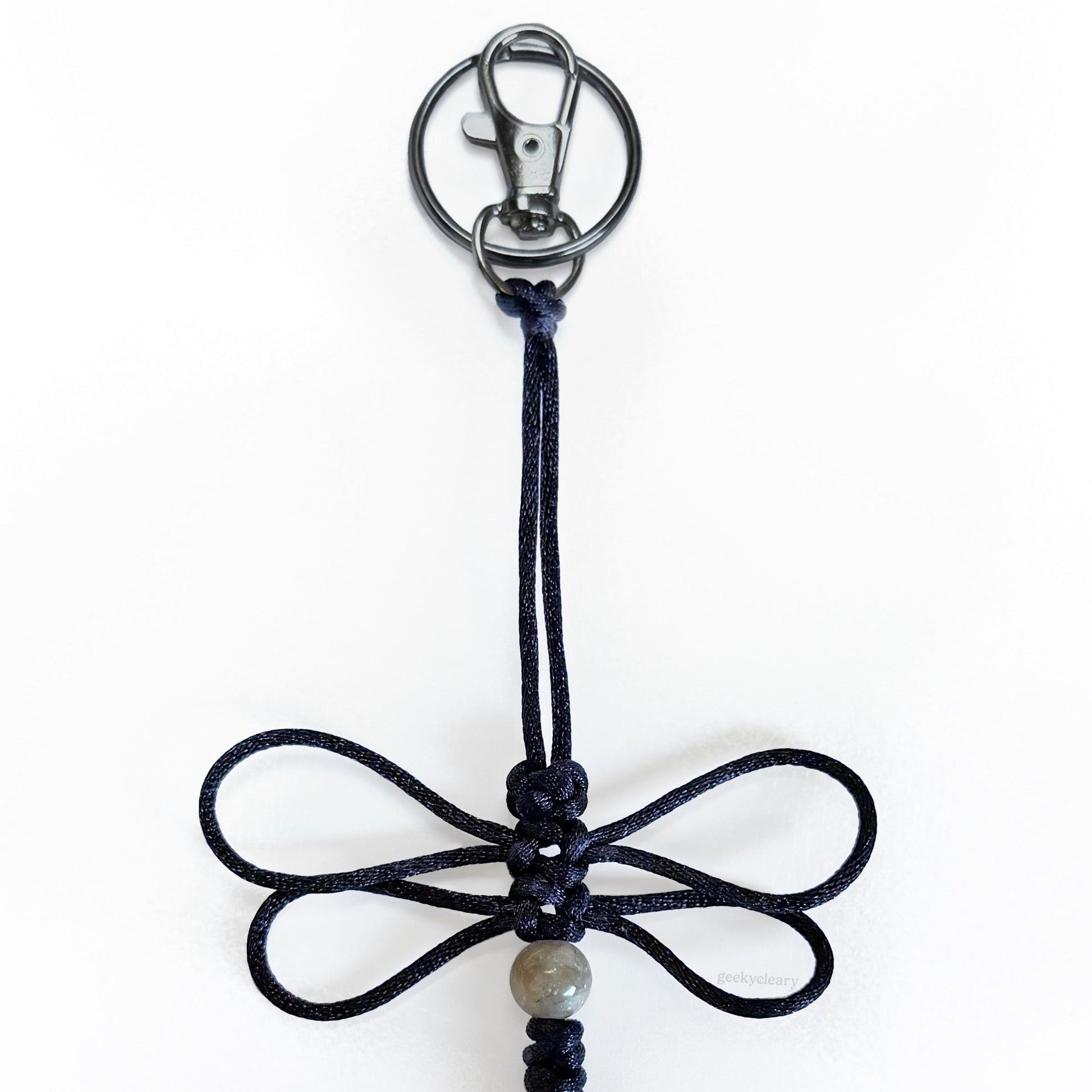 Close up of Nightwing Dragonfly Specimen keychain made of black silk cord, a real agate bead, and silver-toned hardware.
