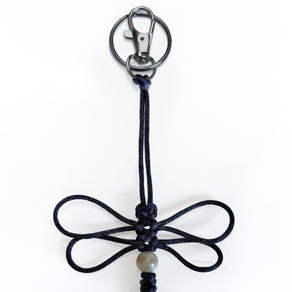 Close up of Nightwing Dragonfly Specimen keychain made of black silk cord, a real agate bead, and silver-toned hardware.