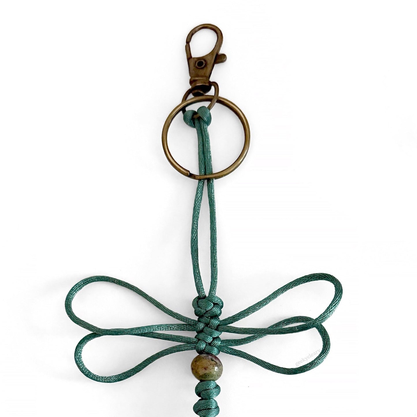 Close up of Verdigris Wing Dragonfly Specimen keychain made of teal silk cord, a real agate bead, and brass-toned hardware.