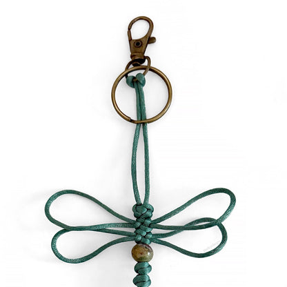 Close up of Verdigris Wing Dragonfly Specimen keychain made of teal silk cord, a real agate bead, and brass-toned hardware.
